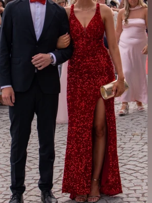 Röd glittrig långklänning med slits - Snygg röd långklänning täckt av paljetter med djup v-ringning och hög slits framtill. Klänningen har smala axelband som korsas och knyts i ryggen för en öppen rygg-effekt. Perfekt för bal eller festliga tillfällen. Klänning är från märket Mascara köpt på Zalando. Hade klänningen på balen förra året så den är endast använd en gång. Storlek 36 😍jag är 178 cm och har klackar på bilderna. Eftersom det är en slits i fram och ett litet släp i bak passar klänningen många beroende på längd.Nypris 2500kr