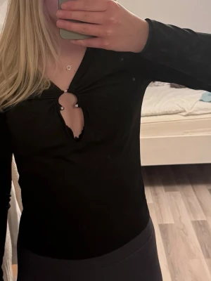 Svart långärmad topp med cut-out - Trendig svart långärmad topp från Bik Bok med snygg cut-out och ringdetalj framtill. Toppen har en åtsittande passform och är tillverkad i mjukt, stretchigt material som känns skönt mot huden. Perfekt för dig som vill ha en stilren men ändå unik look.