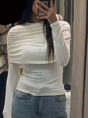 Vit  långärmad topp med ribbade detaljer - Trendig vit långärmad topp med unika ribbade detaljer över axlar och bröst. Figurnära passform och hög hals ger en clean och modern look. Perfekt att styla med jeans eller kjol för en snygg outfit. Använt 1 gång  från Gina 