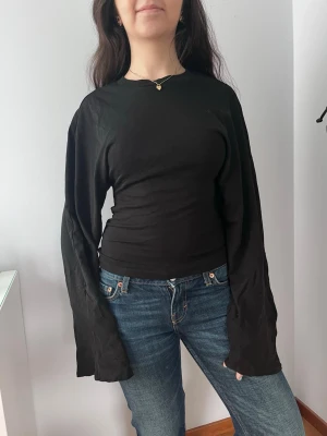Svart långärmad topp från Gina  - En svart långärmad topp från Gina tricot som är tajt vid midjan och har utsvängda armar. Super mjuk och skön. Aldrig använt, prislapp finns kvar💕.