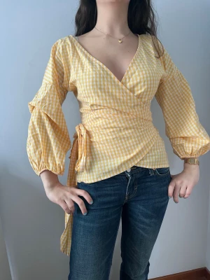 Gulvitrutig omlottblus med puffärm - Supersöt gul och vit rutig omlottblus med puffiga långärmar och knytband i midjan.  Väldigt mjuk och skön i materialet. Nästan helt oanvänd!💕