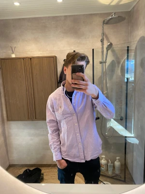 Ljuslila skjorta från Ralph Lauren - Säljer en ljuslila skjorta från Ralph Lauren med klassisk button-down krage och broderad logga på bröstet. Skjortan har långa ärmar, knappar framtill och är tillverkad i mjuk bomull. Perfekt för en clean och stilren look.