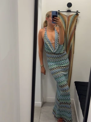 Missoni långklänning med djup urringning - Säljer en långklänning med färgglatt zickzack-mönster i blått, grönt, vitt och svart. Klänningen har djup v-ringning, halterneck och är ärmlös. Ryggen är en djup öppning. Materialet är stretchigt och lätt, perfekt för varma dagar. Storleken är S/M och passar de flesta. Aldrig använd!! Nypris 100€