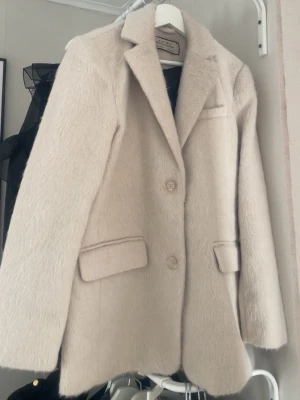 Beige ullkappa  - Snygg beige kappa med två knappar framtill, klassisk krage och två fickor med lock. Kappan har en rak passform och mjuk, lite lurvig yta som ger en trendig look. Perfekt för kyliga dagar och enkel att styla till olika outfits. Kappan är oversize och passar någon som har storlek s/m💗💕(jackan är använd en gång)