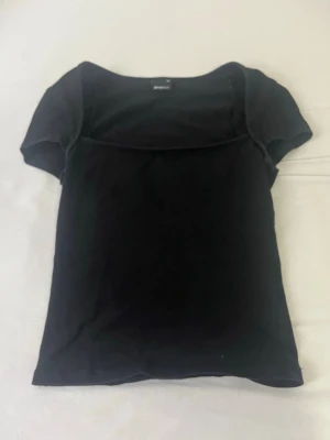 Svart kortärmad topp Gina Tricot - En enkel svart topp från Gina Tricot med korta ärmar och rundad halsringning. Modellen är figurnära och passar perfekt till jeans eller kjol. Tillverkad i mjukt bomullsmaterial för en bekväm känsla.