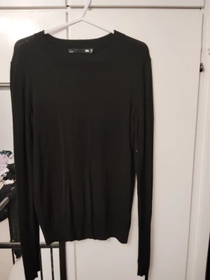 Svart stickad tröja med rund hals - En enkel och stilren svart stickad tröja med rund halsringning och långa ärmar. Tröjan har en smal passform och ribbade muddar vid ärmslut och nederkant. Perfekt basplagg för lager på lager och passar till det mesta.