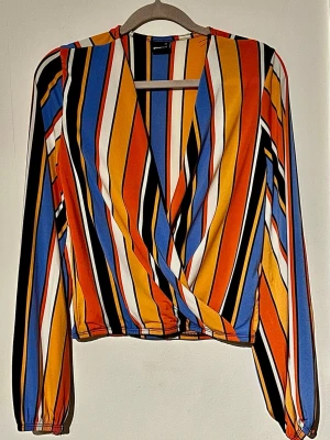 🔥 Gina Tricot omlott topp XS – färgglad statement 🔥 - Använd 1 gång – i princip nyskick ✨ Scroll-stopper topp som verkligen sticker ut 🔥  💥 Stretchig & sitter perfekt 💥 Smickrande omlott-modell 💥 Perfekt till både vardag & fest 👚 Detaljer: 	•	XS 	•	Gina Tricot 	•	Croppad modell 	•	Mycket fint skick  📏 Mått: 	•	Byst: ca 37 cm 	•	Ärmlängd: ca 37 cm 	•	Armbredd: ca 26 cm