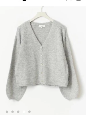 Ljusgrå kofta med v-ringning - Mysig ljusgrå kofta med v-ringning och knappar framtill. Koftan har en avslappnad passform, långa ärmar och är stickad i ett mjukt material som känns fluffigt. Perfekt att slänga på sig när det är lite kyligt ute.