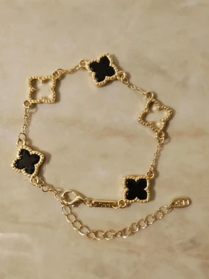 Guldfärgat armband med svarta klöver✨🖤 - Stilrent armband i guldfärg med dekorativa fyrklöverformade länkar, varav tre är fyllda med svart emalj och två är öppna. Justerbar kedja och elegant design som sticker ut✨