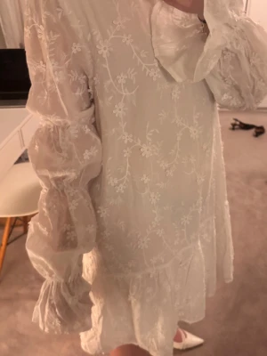 Vit klänning från nakd - Söt vit kortklänning med broderade blommor och volangkant. Klänningen har långa puffärmar med resår vid ärmslut och en lös passform. Perfekt för sommarens alla tillfällen och ger en romantisk vibe. Prislappen är kvar och klänningen är endast provad!!