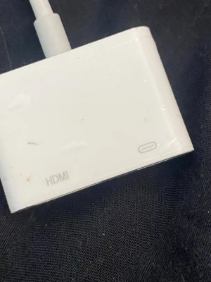 Vit HDMI-adapter med USB-C - En vit HDMI-adapter med USB-C-port, perfekt för att koppla dator eller surfplatta till en skärm eller TV. Kompakt och rektangulär form, tillverkad i plast. Enkel att använda för att få bild och ljud via HDMI.