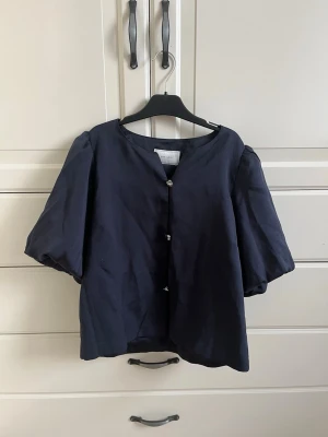 Neo noir blus - Säljer en superfin svart satinblus med korta puffärmar och dekorativa knappar framtill från Neo Noir. Passar både till vardag och fest. Mycket bra skick, sparsamt använd. Storlek xs🩷