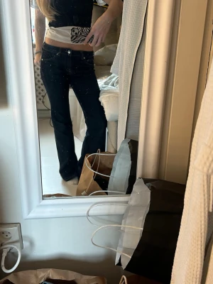 Mörkblå bootcut jeans - Säljer ett par mörkblå bootcut jeans med låg midja och klassiska fem fickor. Jeansen har en snygg utsvängd passform och är perfekta för en trendig vardagslook. Materialet är denim i bomull med lite stretch för extra komfort.