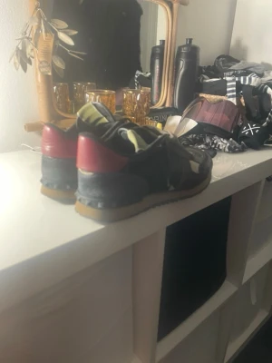Valentino rockrunner sneakers med röd häl - Snygga sneakers från Valentino med camomönster i grönt, svart och beige. Skorna har en röd detalj på hälen, guldfärgad logga på plösen och beige sula. Materialmix av mocka, läder och textil ger en cool och unik look.