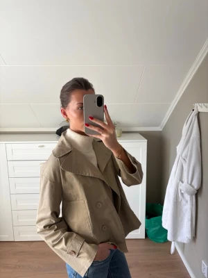 Kort trenchcoat  - Kort trencoat från Design By Si (modell Via), storlek XS/S. I mycket bra skick.