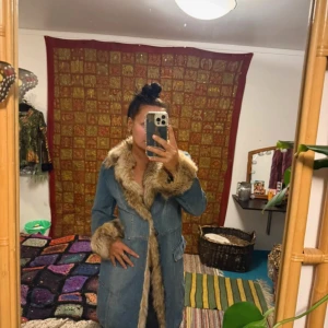 Vintage jeansjacka med pälsdetaljer - Säljer en unik vintage jeansjacka med fluffiga pälsdetaljer i beige längs krage, ärmslut och framkant. Jackan har stora fickor, markerad midja och snygga knappar framtill. Perfekt för dig som vill sticka ut med retrovibe och cool 70-talsstil. Några fläckar som jag inte testat ta bort..se sista bilden.