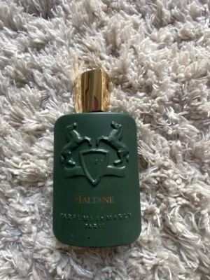 Parfums de Marly Haltane EdP 125ml - Lyxig parfym från Parfums de Marly, Haltane, i en elegant grön flaska med gulddetaljer och reliefmönster av hästar. Kommer i matchande grön och guld kartong. Doften är en del av Royal Essence-kollektionen och utstrålar exklusivitet.