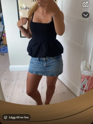 Svart peplum linnetopp - Säljer en svart linnetopp med breda axelband och peplumvolang nedtill. Toppen har en enkel och stilren design som passar perfekt till jeans eller kjol. Materialet känns lätt och luftigt, perfekt för varma dagar.