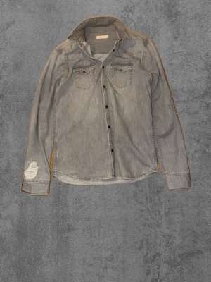 Grå skjorta/overshirt med slitningar - Snygg grå skjorta med två bröstfickor och slitna detaljer på ärmarna. Klassisk krage och knäppning framtill. Perfekt för dig som gillar en avslappnad och trendig stil.