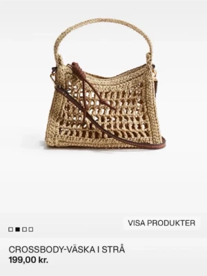 Beige axelväska i strå med flätad design - Säljer en beige axelväska i strå med öppen, flätad design och bruna detaljer. Väskan har både handtag och justerbar axelrem i brunt läderimitation. Perfekt för dig som gillar en bohemisk och trendig look.