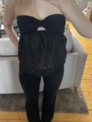 Svart axelbandslös bandeautopp - Snygg svart bandeautopp med twistad byst och liten cut-out framtill. Toppen är axelbandslös och har ett broderat blommönster på nederdelen. Finns ingen lapp med tror storlek xs. Aldrig använd 