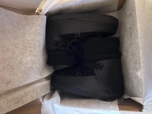 Svarta boots från Inuikii NYA - Säljer ett par svarta moon boots från Inuikii med klassisk rundad form och snörning framtill. Skorna har en robust sula med bra grepp och är tillverkade i ett tåligt material som passar perfekt för kalla dagar. Snygg och stilren design som funkar till många outfits. Äkta, köpta nya utav mig.