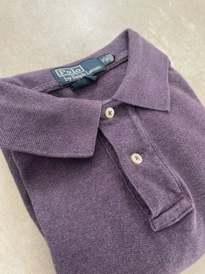 Lila långärmad piké från Polo Ralph Lauren - Säljer en lila långärmad pikétröja från Polo Ralph Lauren med klassisk krage och två knappar framtill. Tröjan har diskret logga broderad på bröstet och är gjord i mjukt bomullsmaterial. Perfekt för en avslappnad men ändå stilren look. Mått 📏 Längd från axel: 68cm Axelbredd: 44cm Skador 🔧: Inga  Storlek 🧍: M  Passform: Custom fit  Jag kan förhandla mig till lägre pris.🙋💵 Om du har några frågor, vänligen skriv till mig 🤗