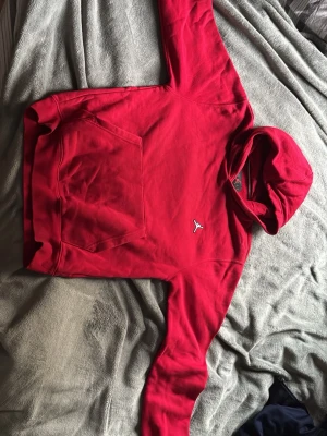 Röd Jordan hoodie med logga - Snygg röd hoodie från Jordan med klassisk Jumpman-logga broderad på bröstet. Hoodien har en stor magficka och huva. Perfekt för dig som gillar streetwear och sportig stil. Materialet är mjukt och bekvämt bomullstyg.