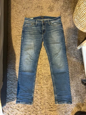 Clark jeans från Jacknjones - Säljer ett par klassiska blå jeans från Jack n Jones med rak passform och snygg slitning på framsidan. Jeansen har fem fickor, normal midja och är gjorda i mjuk denim. Perfekta för en avslappnad och stilren look. Bara använd fåtal gånger 