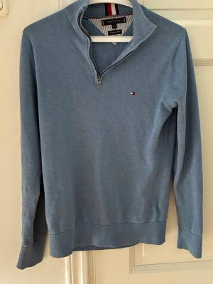 Blå halvzip-tröja Tommy Hilfiger - Snygg blå långärmad tröja från Tommy Hilfiger i premium bomull. Halvzip-modell med liten broderad logga på bröstet och ribbade muddar vid ärmslut och nederkant. Perfekt för en stilren och avslappnad look. Nypris ca 800