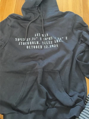 Svart hoodie Ant Wan Tele2 Arena - Säljer min Antwan tröja då jag aldrig har använt den. Svart hoodie med stor färgglad grafisk print på ryggen och vit text på bröstet. Texten inkluderar koordinater, Stockholm, Tele2 Arena och datum. Klassisk känguruficka och dragsko i huvan. Perfekt för dig som gillar streetweary och unika plagg. 