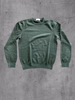 Grön stickad tröja från Gran Sasso - Snyggt stickad tröja i dämpad grön färg från Gran Sasso. Klassisk rund halsringning och ribbade muddar vid ärmslut och nederkant. Tillverkad i Italien, mjukt material som känns lyxigt och passar perfekt till lager på lager. Storlek 46 italiensk storlek motsvarar ca S