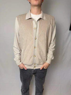 Gran Sasso cardigan - Stilren beige cardigan från Gran Sasso med klassisk krage och knäppning framtill. Tröjan har långa ärmar, ribbade muddar och två fickor framtill. Perfekt för en clean och avslappnad look. Modellen på bilden är 182cm och väger 80kg. Storlek 54 sitter som L