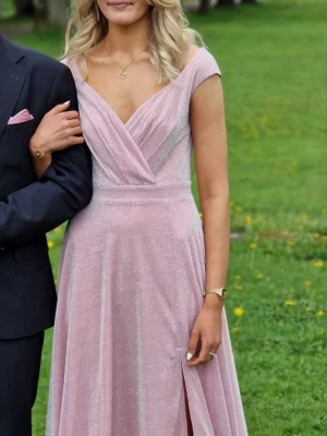 Ljusrosa glittrig balklänning med slits - Elegant ljusrosa balklänning med v-ringad omlottdesign och glittrigt tyg. Klänningen har cap-ärmar och en hög slits framtill som ger en snygg touch. Jag är 178 och den var perfekt med låga klackar! Verkligen super vacker klänning! Men säljer då jag köpt en annan till min studentbal. Endast använd en gång på en bal för 2 år sen!