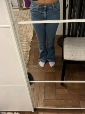 Blå bootcut jeans med hög midja - Säljer ett par ljusblå bootcut jeans med hög midja och klassisk femficksdesign. Jeansen har en snygg passform som sitter tajt över höfterna och släpper ut vid benen. Tillverkade i ett mjukt denimtyg som är bekvämt att bära.