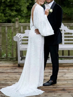 Vit långklänning med öppen rygg - Elegant vit långklänning med glittriga paljetter, djup öppen rygg och vida ärmar. Klänningen har en figurnära passform och ett långt släp som ger en lyxig känsla. Perfekt för dig som vill sticka ut på speciella tillfällen. Prislapp kvar 