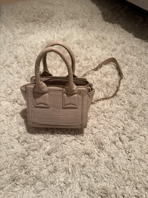 Beige miniväska från Zara - Snygg beige miniväska från Zara med croco-mönster och guldfärgad kedjerem. Väskan har två handtag och dragkedja upptill. Perfekt för att bära det viktigaste🔥✨
