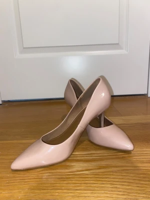 Beige/rosa spets pumps  - Snygga pumps i ljusrosa/beige med spetsig tå och smal klack. Skorna har en stilren och klassisk design som passar till många  outfits. Tillverkade i syntetmaterial med en glansig finish. Perfekta för dig som gillar en elegant look. En sko har ett litet märke som man ser på tredje bilden, vet inte om de går att tvätta bort! 