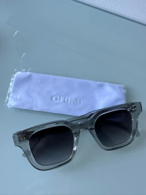 Chimi solglasögon grey 04  - Snygga solglasögon med transparent, fyrkantig båge och mörka glas. Riktigt trendig modell som passar alla modeller. Glasögonen är från chimi och är i färgen grå 04. Har inga repor eller liknande, ser ut som nya. 