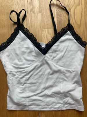 Vit linnetopp med spetskant - Söt vit linnetopp med svarta justerbara axelband och svart spetskant längs urringningen. Lite noppring. 