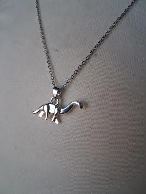 Halsband med dinosaurieberlock i silver - Snyggt halsband med en silverfärgad kedja och en berlock formad som en dinosaurie. Berlocken har fina detaljer och ger ett lekfullt intryck. Perfekt för dig som gillar unika smycken och vill sticka ut lite extra.