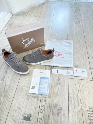 Gråa Louboutin sneakers i mocka - Snygga gråa sneakers från Christian Louboutin i mjuk mocka med vita sulor och klassisk röd detalj på insidan. Lågt skaft och neutrala snören ger en clean look. Kommer med originalkartong och dustbag. Priset är inte hugget i sten, hör av er vid frågor