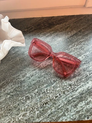 Rosa Chimi solglasögon - Snygga solglasögon i transparent rosa med bred båge och stora glas. Den fyrkantiga formen ger en trendig vibe och de passar perfekt för dig som vill sticka ut i vår och sommar.