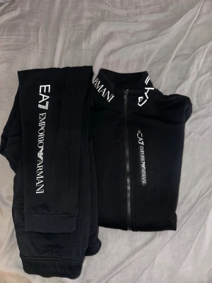 Emporio Armani sett  - Snyggt svart loungewear-set från Emporio Armani EA7 med dragkedja på tröjan och tydliga logotyper på både byxa och tröja. Setet har hög krage med tryckt logga.  Mycket bra sick precis som ny. Ny pris 1750 kr 