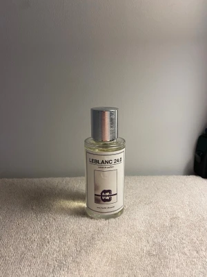 LEBLANC 24.0 Extrait de Parfum - LEBLANC 24.0 Extrait de Parfum kommer i en stilren, genomskinlig glasflaska med metalliskt silverlock och sprayfunktion. Etiketten är minimalistisk med svart text och en grafisk symbol i lila. Perfekt för dig som gillar exklusiva och moderna dofter.