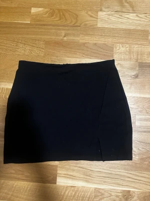 Svart kortkjol från Windsor - En stilren svart kortkjol från Windsor med enkel design och liten slits framtill. Kjolen har en tight passform och är perfekt för dig som gillar minimalistisk stil. Tillverkad i mjukt och stretchigt material för extra komfort. Ganska kort!