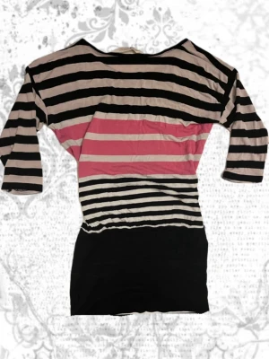 Randig topp med trekvartsärm - Snygg randig topp med svarta, beige och rosa ränder. Modellen har trekvartsärm och båtringad hals. 