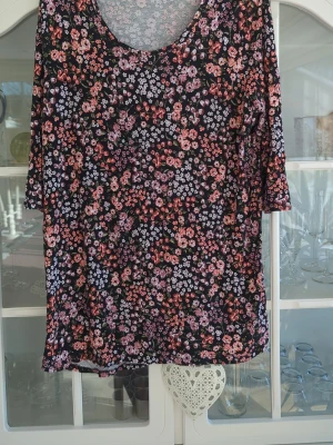 Blommig topp med trekvartsärm - Snygg topp med svart botten och tätt blommönster i rosa, lila och röda toner. Modellen har rund halsringning och trekvartsärm. Perfekt för dig som gillar färg och mönster i din vardagsstil.