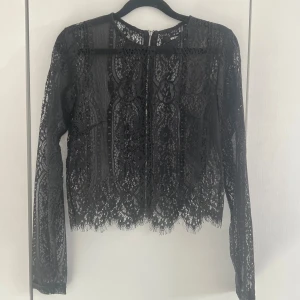 Svart spetsblus  - Säljer en svart, långärmad spetsblus med vackra spetsdetaljer och rund hals. Blusen har en rak passform och dragkedja i ryggen. Perfekt för dig som gillar en elegant och trendig look.