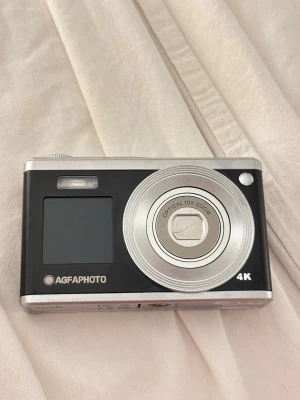 AgfaPhoto digitalkamera 4K svart/silver - Snygg digitalkamera från AgfaPhoto i svart och silver med 4K-upplösning och optisk 10x zoom. Kameran har en kompakt, rektangulär form och tydlig display på baksidan. Perfekt för dig som vill ta skarpa bilder och filmer med stilren design. Modell DC9200. Köpt i Juli 2025. Nypris ca 1500kr. Knappt använd. Tar jättefina bilder!!! Kan skicka på förfrågan